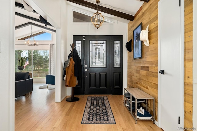entrance foyer with an inviting chandelier, light wood finished floors, wooden walls, and vaulted ceiling with beams