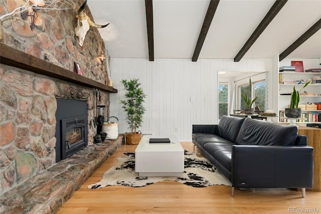 living area with a stone fireplace, wood finished floors, and beamed ceiling