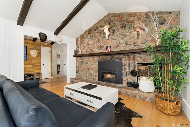 living room featuring vaulted ceiling with beams, a stone fireplace, wood walls, and wood finished floors