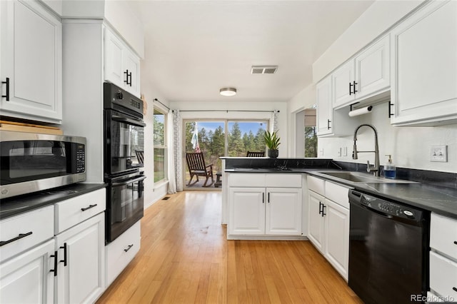 kitchen with white cabinets, dark countertops, a sink, and black appliances