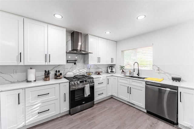 7302 E Bates Dr, Denver, CO 80231 - kitchen with stainless steel appliances, wall chimney exhaust hood, decorative backsplash, white cabinets, and light wood-style floors