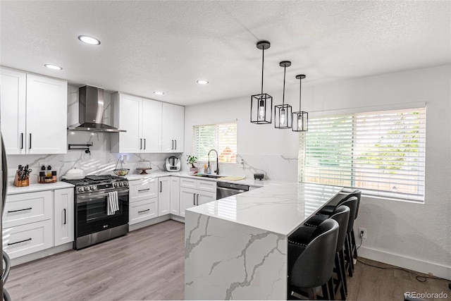 7302 E Bates Dr, Denver, CO 80231 - kitchen with wall chimney range hood, appliances with stainless steel finishes, a peninsula, light wood-style floors, and a textured ceiling