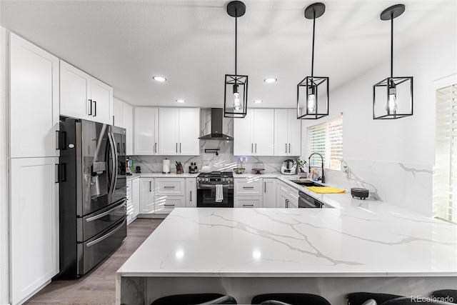 7302 E Bates Dr, Denver, CO 80231 - kitchen with appliances with stainless steel finishes, wall chimney range hood, a peninsula, wood finished floors, and light stone counters
