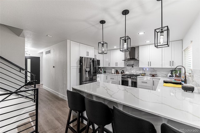 7302 E Bates Dr, Denver, CO 80231 - kitchen with wall chimney range hood, appliances with stainless steel finishes, a peninsula, light stone countertops, and white cabinetry