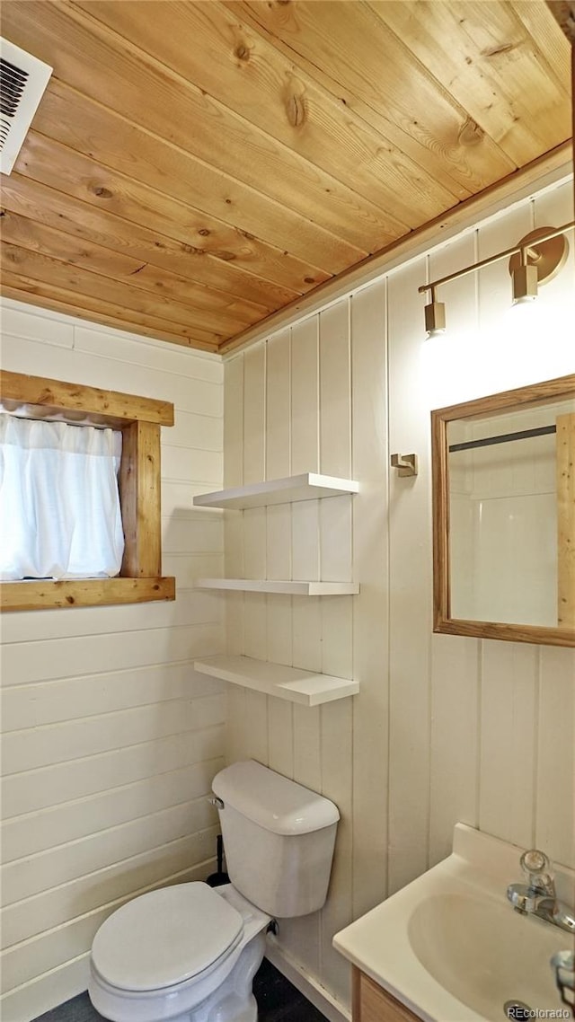 bathroom with toilet, wood walls, vanity, and wooden ceiling