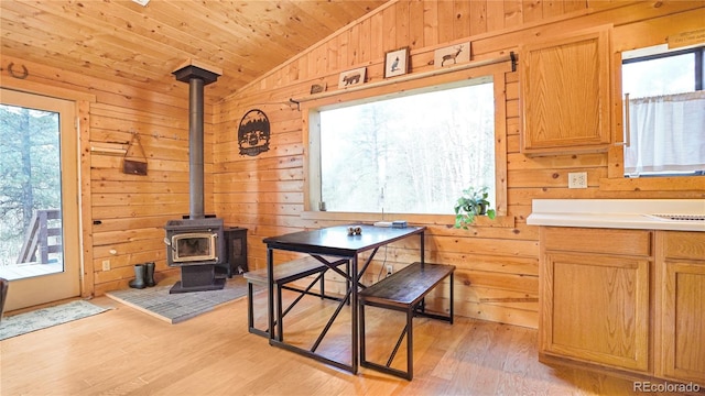 dining area featuring wooden walls, vaulted ceiling, light wood-type flooring, and a wood stove