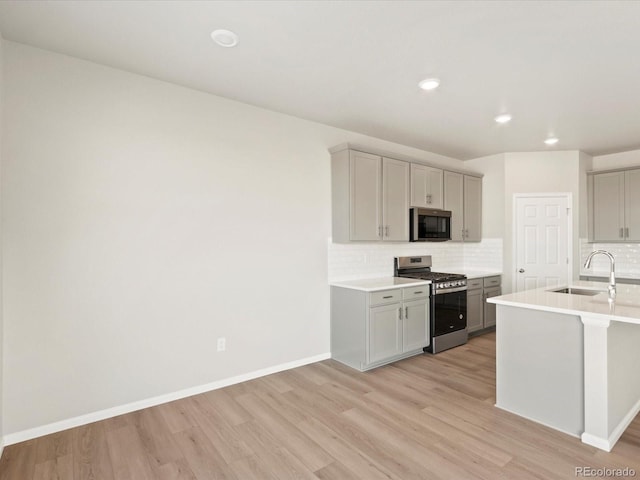 kitchen with gray cabinetry, light wood-style flooring, a sink, backsplash, and stainless steel appliances