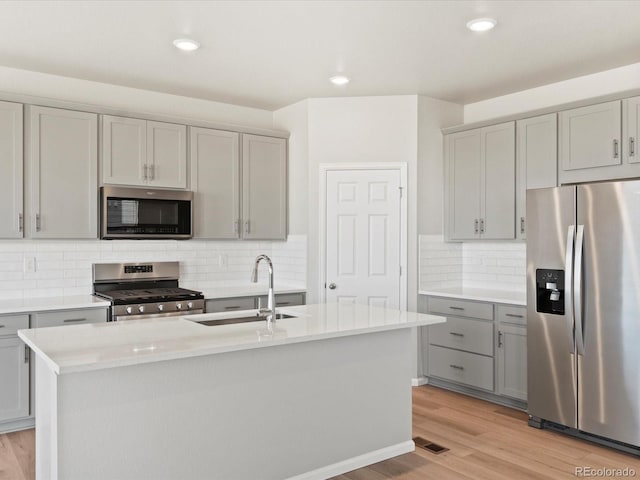 kitchen featuring light wood-style flooring, gray cabinets, a sink, light countertops, and appliances with stainless steel finishes