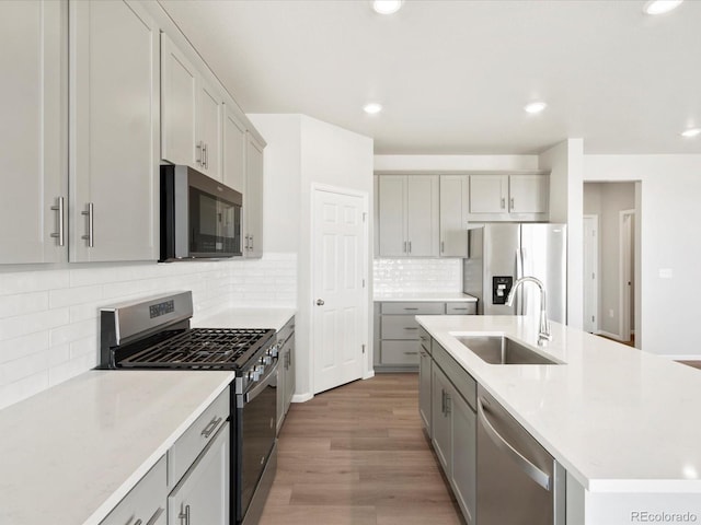 kitchen with a center island with sink, light wood-type flooring, gray cabinets, stainless steel appliances, and a sink