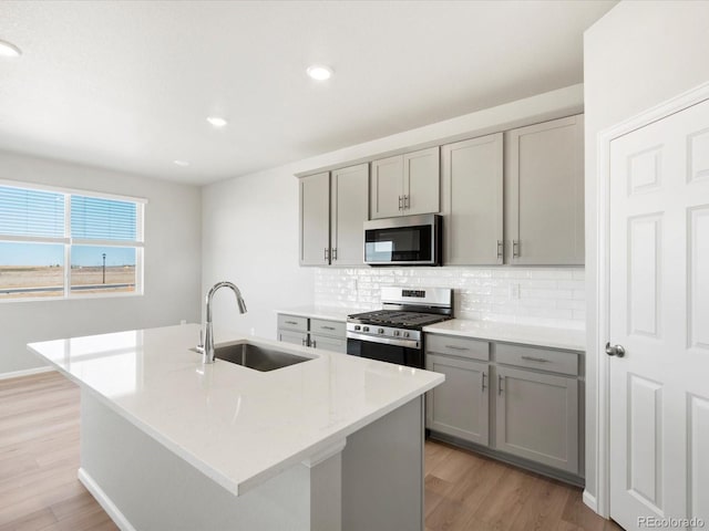 kitchen with light wood-type flooring, gray cabinets, a sink, tasteful backsplash, and appliances with stainless steel finishes