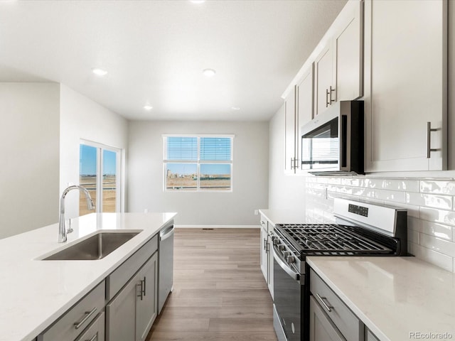 kitchen featuring a sink, gray cabinets, backsplash, and stainless steel appliances