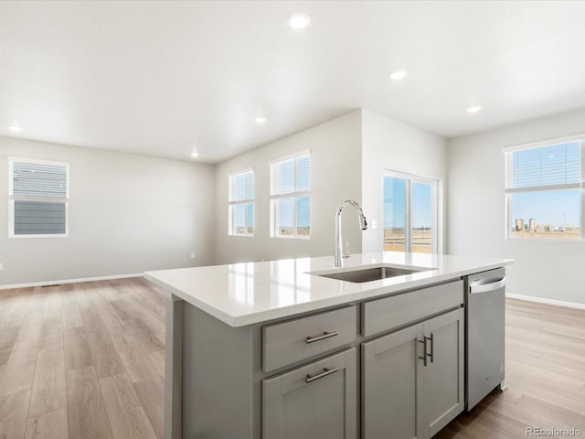 kitchen featuring a center island with sink, light wood-style flooring, a sink, light countertops, and stainless steel dishwasher