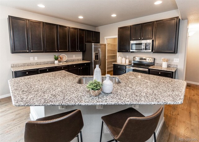 kitchen with a kitchen breakfast bar, dark brown cabinetry, an island with sink, and appliances with stainless steel finishes