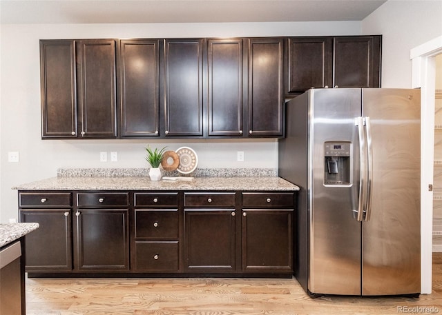 kitchen featuring stainless steel fridge, light wood-type flooring, light stone counters, and dark brown cabinetry