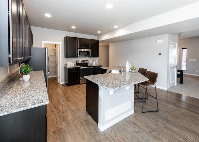 kitchen featuring a breakfast bar, a kitchen island with sink, sink, light hardwood / wood-style flooring, and appliances with stainless steel finishes