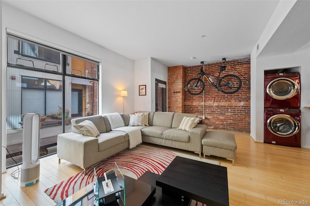 living area with stacked washer / dryer, brick wall, and wood finished floors