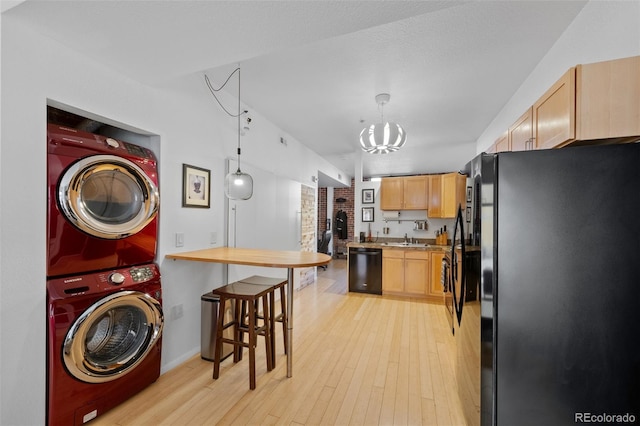 laundry area with laundry area, light wood-style flooring, a sink, stacked washer and clothes dryer, and a notable chandelier