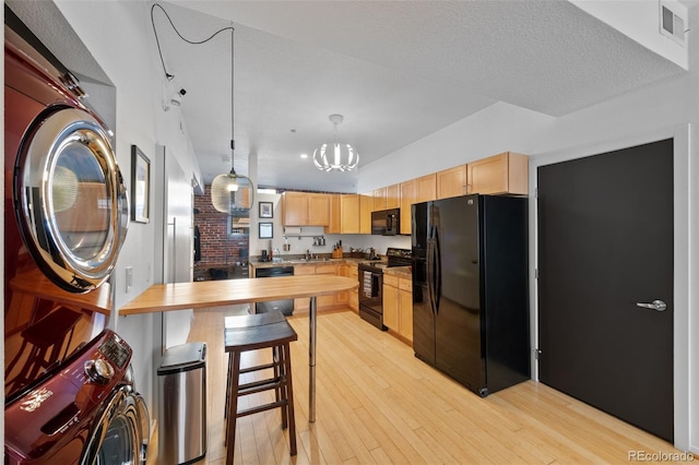 kitchen featuring light brown cabinets, visible vents, stacked washing maching and dryer, black appliances, and light wood-style floors