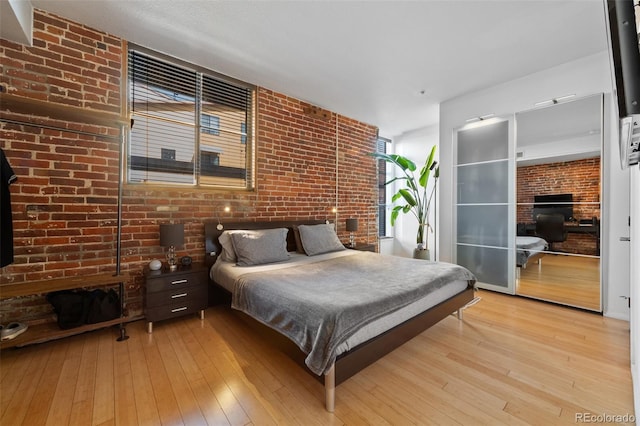 bedroom featuring light wood-style floors and brick wall