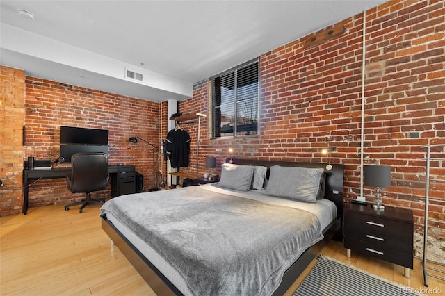 bedroom with visible vents, brick wall, and wood-type flooring