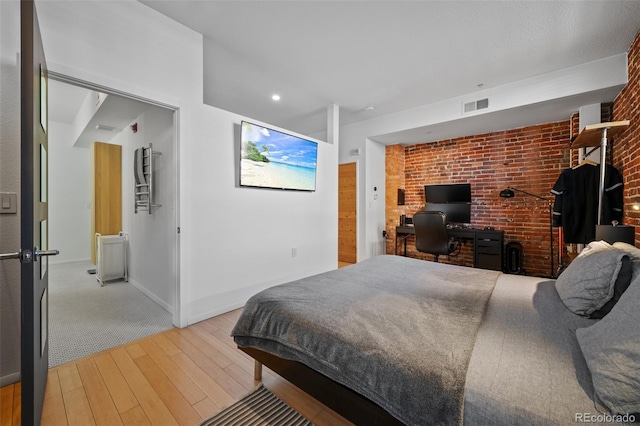 bedroom featuring visible vents, baseboards, brick wall, and light wood finished floors