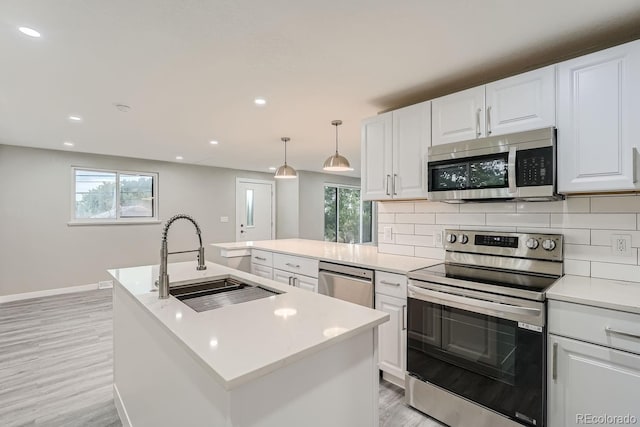 kitchen with pendant lighting, sink, appliances with stainless steel finishes, a kitchen island with sink, and white cabinetry