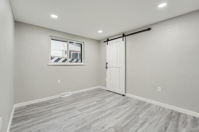 unfurnished room featuring a barn door and light hardwood / wood-style floors