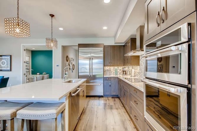 kitchen featuring backsplash, a kitchen breakfast bar, appliances with stainless steel finishes, decorative light fixtures, and light hardwood / wood-style floors