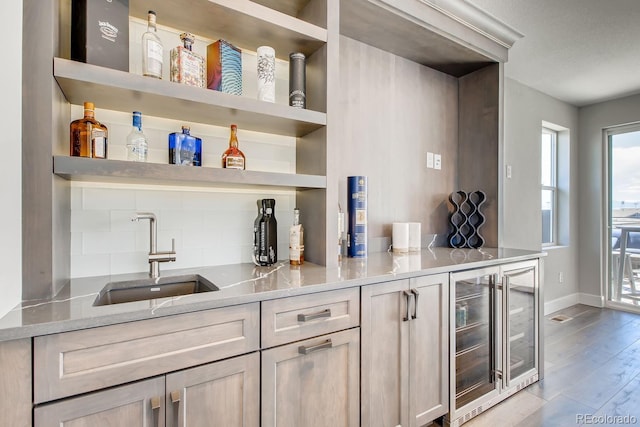 bar featuring light stone countertops, light brown cabinetry, beverage cooler, sink, and light hardwood / wood-style floors