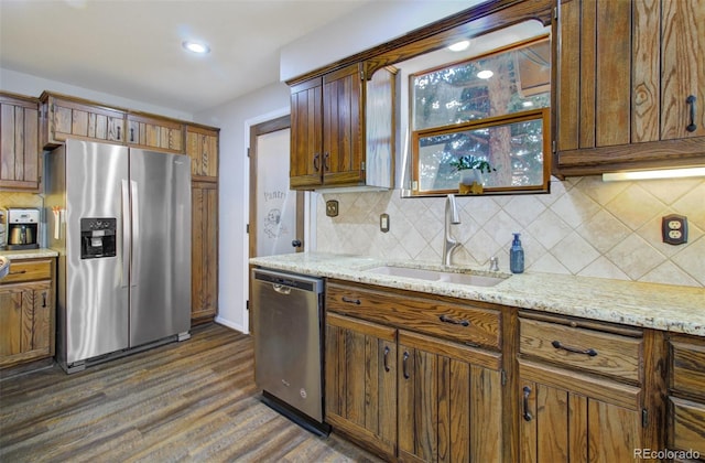 kitchen featuring appliances with stainless steel finishes, a sink, dark wood-style floors, backsplash, and light stone countertops