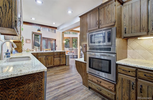 kitchen featuring appliances with stainless steel finishes, a sink, a peninsula, decorative backsplash, and light wood-type flooring