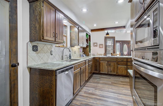 kitchen featuring stainless steel appliances, a sink, light wood finished floors, backsplash, and recessed lighting