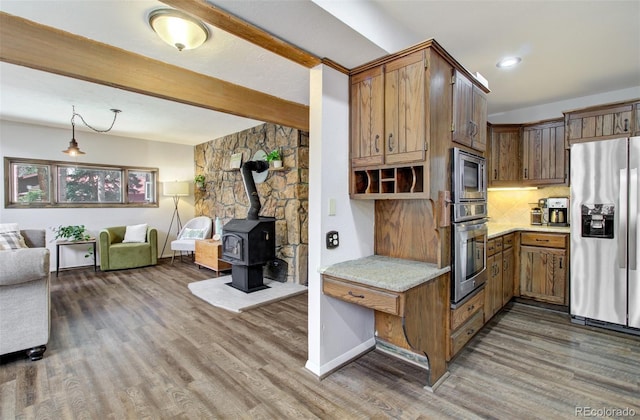 kitchen with appliances with stainless steel finishes, open floor plan, wood finished floors, beam ceiling, and a wood stove