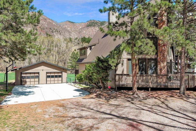 view of property exterior with an outdoor structure, a detached garage, a deck with mountain view, and a chimney