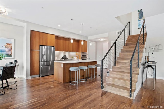 kitchen with appliances with stainless steel finishes, a breakfast bar, pendant lighting, wood-type flooring, and a center island with sink