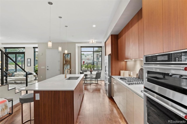 kitchen with backsplash, a kitchen island with sink, hanging light fixtures, sink, and appliances with stainless steel finishes