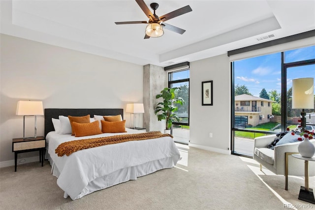 carpeted bedroom with ceiling fan, access to exterior, and a tray ceiling