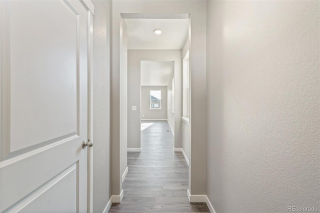 hall featuring dark wood-style floors, baseboards, and a textured wall