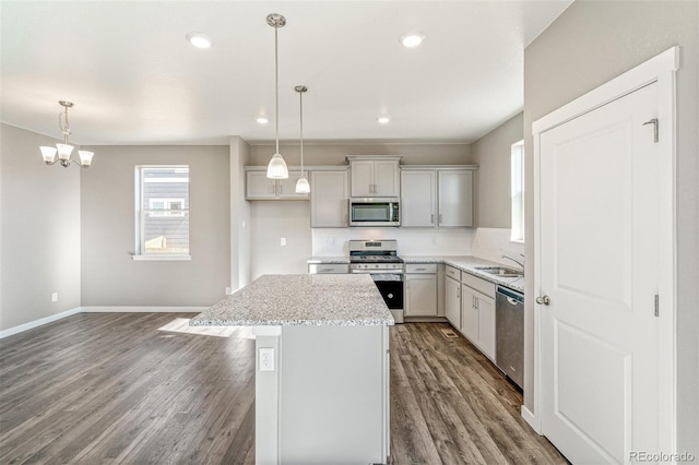 kitchen with a sink, a kitchen island, baseboards, appliances with stainless steel finishes, and dark wood-style flooring