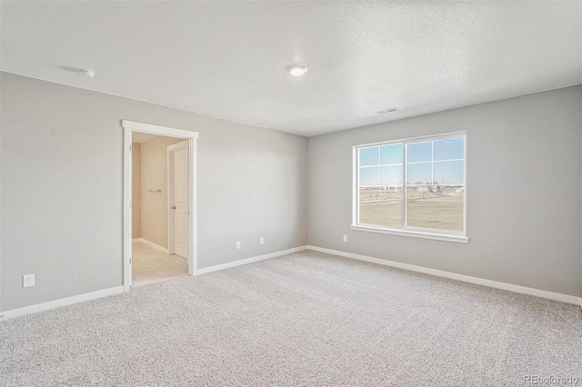 spare room featuring visible vents, baseboards, light colored carpet, and a textured ceiling