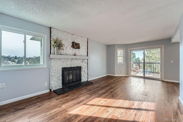 unfurnished living room with a wealth of natural light, a stone fireplace, hardwood / wood-style floors, and baseboards