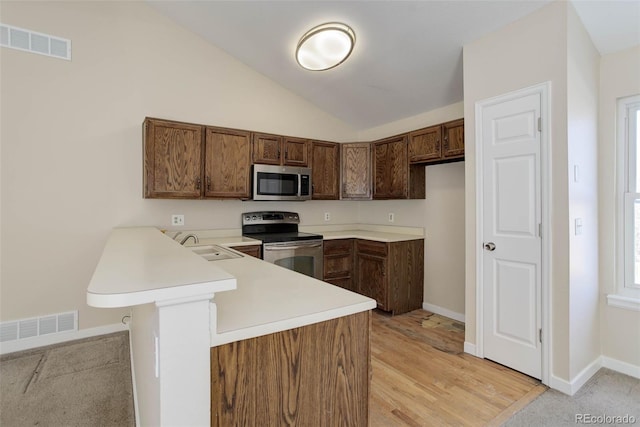 kitchen with a breakfast bar, light hardwood / wood-style flooring, vaulted ceiling, appliances with stainless steel finishes, and kitchen peninsula