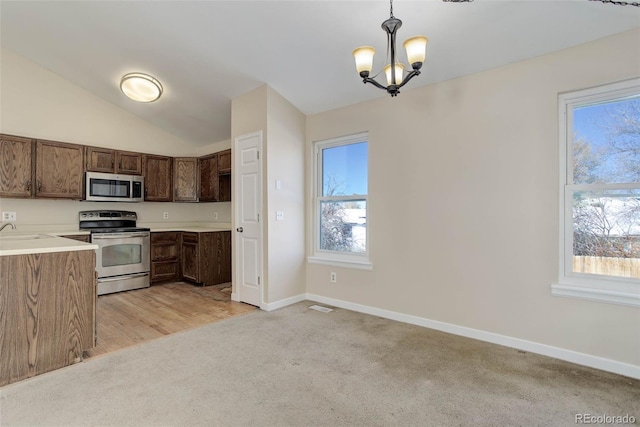 kitchen with lofted ceiling, stainless steel appliances, hanging light fixtures, and a healthy amount of sunlight