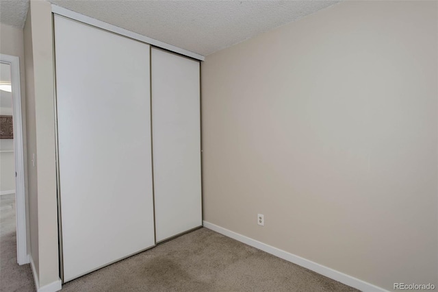 unfurnished bedroom with a closet, light colored carpet, and a textured ceiling