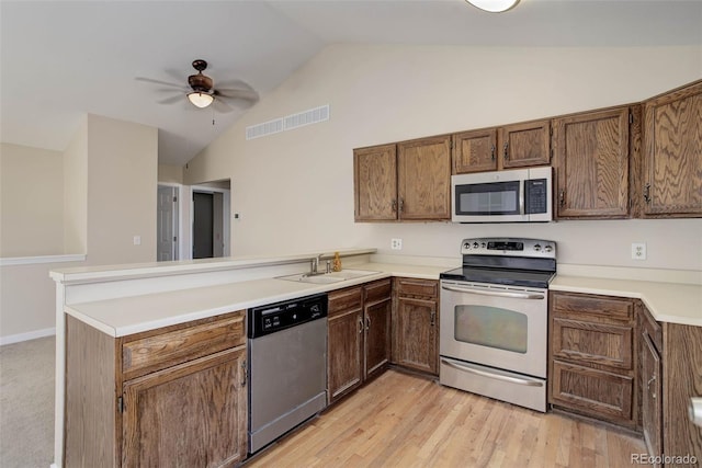 kitchen featuring kitchen peninsula, appliances with stainless steel finishes, light wood-type flooring, vaulted ceiling, and sink