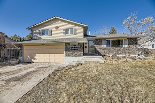 tri-level home featuring a garage, stone siding, fence, and driveway