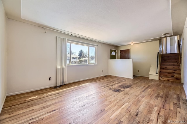 empty room with wood-type flooring, stairs, baseboards, and visible vents