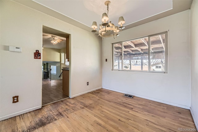 empty room featuring baseboards, visible vents, wood finished floors, and ceiling fan with notable chandelier