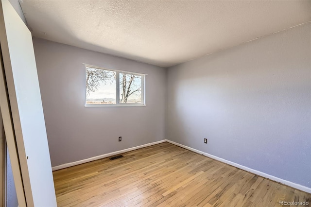 empty room featuring a textured ceiling, hardwood / wood-style floors, visible vents, and baseboards