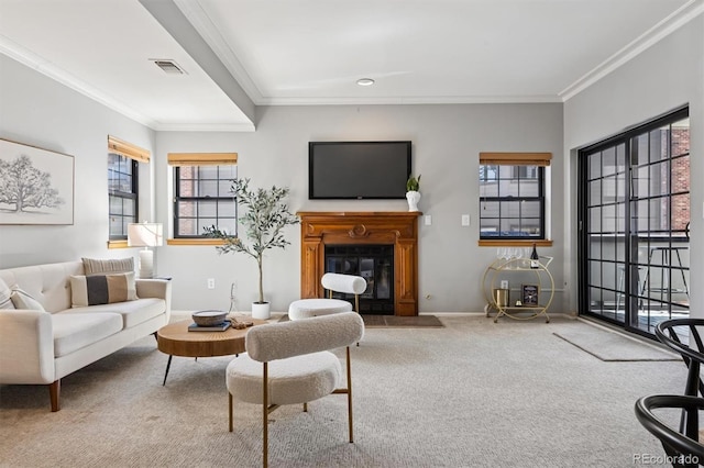 carpeted living area with visible vents, ornamental molding, baseboards, and a glass covered fireplace